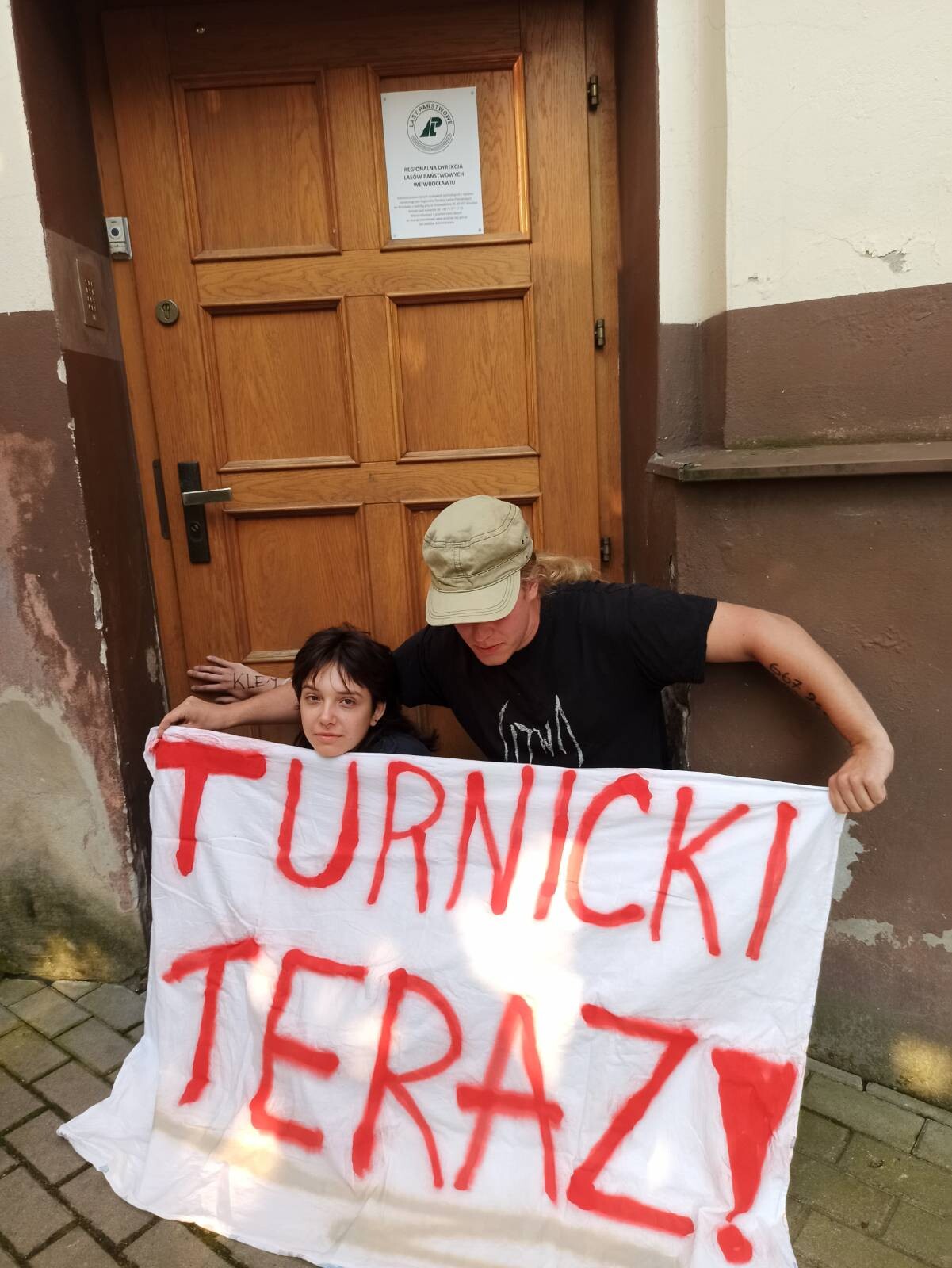 Aktywiści przyklejeni do drzwi RDLP z banerem "Turnicki Teraz!"