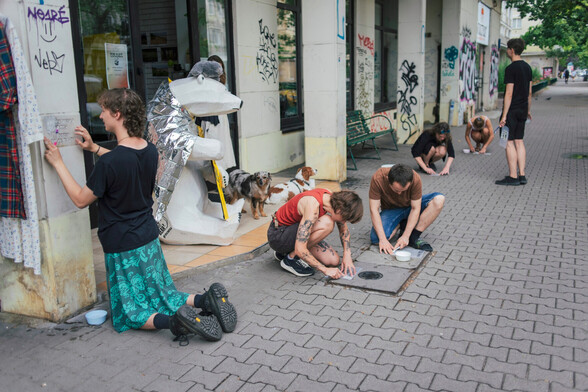 Uczestnicy warsztatów ze streetartu robiący napisy poprzez czyszczenie brudnej powierzchni przez szablon.