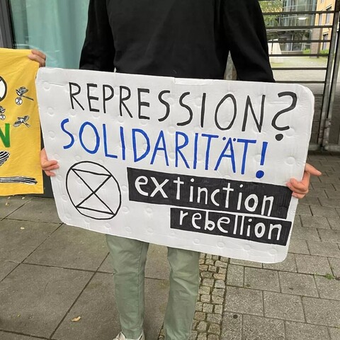 Ein Mensche hält ein Schild mit den Text:
"Repression?
Solidarität!
Extinction Rebellion"