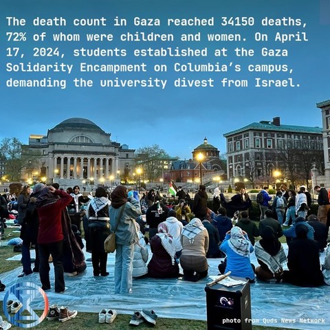 Photo from Quds news network. Gathering on lawn in front of Colombia University, twilight. Some of the people in the foreground are kneeling as if in prayer. Many are wearing the black and white keffiyeh scarf.