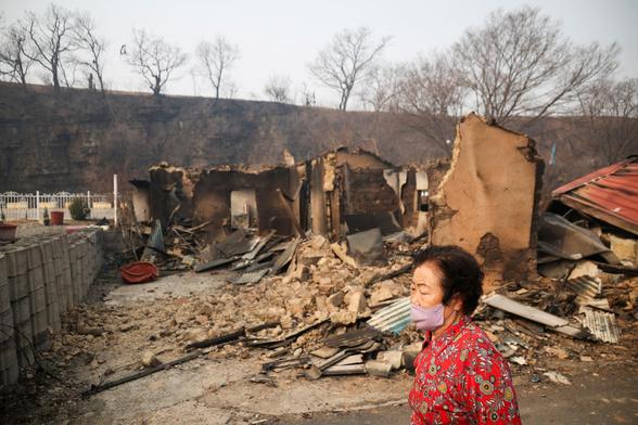 a person walks past fire destroyed buildings.