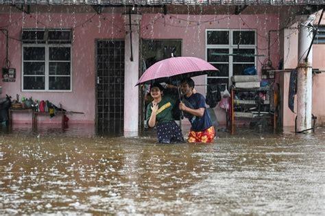 People with an umbrella walking through almost waist high water in a flooded street.